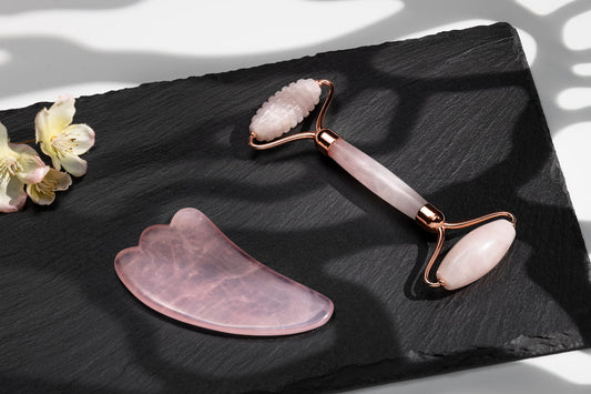 Rose quartz facial roller and gua sha stone set on a styled surface
